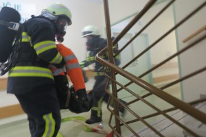 Gasilci prenašajo poškodovano osebo po stopnicah.